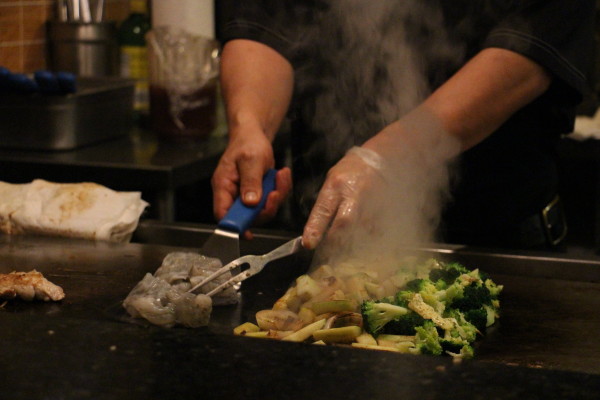 A cook grills raw vegetables and cold shrimp for customers waiting in the dining room. Photo by Courtney Stringfellow. 
