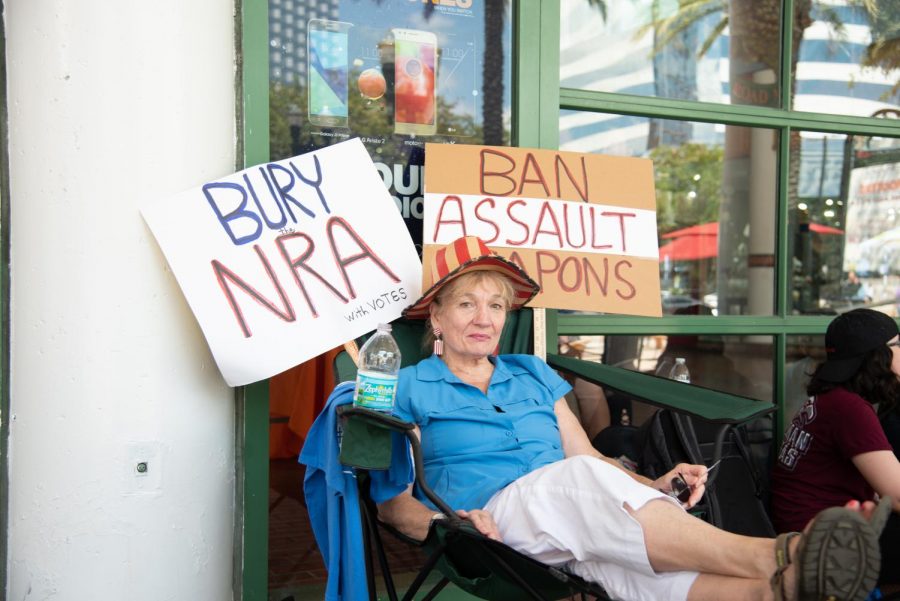 A protestor holds signs saying to "Bury the NRA" and "Ban Assault Weapons."