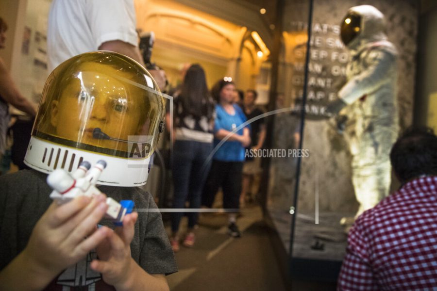 Jack Heely, 5, of Alexandria, Va., wears a toy space helmet as he arrives as one of the first visitors to view Neil Armstrongs Apollo 11 spacesuit, background, after it is unveiled at the Smithsonians National Air and Space Museum on the National Mall in Washington, Tuesday, July 16, 2019. (AP Photo/Andrew Harnik)
