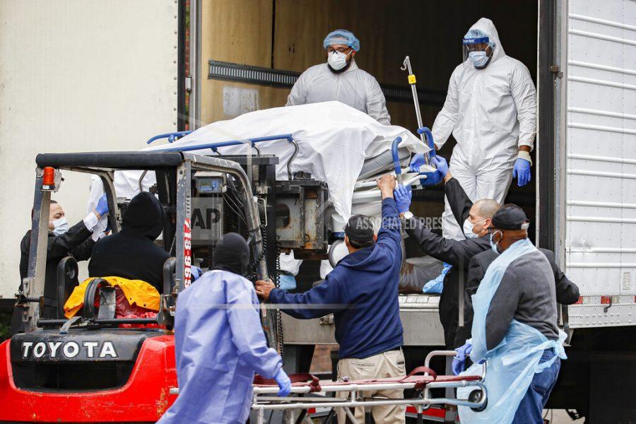A body wrapped in plastic is unloaded from a refrigerated truck and handled by medical workers wearing personal protective equipment due to COVID-19 concerns, Tuesday, March 31, 2020, at Brooklyn Hospital Center in the Brooklyn borough of New York. The body was moved to a hearse to be removed to a mortuary. The new coronavirus causes mild or moderate symptoms for most people, but for some, especially older adults and people with existing health problems, it can cause more severe illness or death. (AP Photo/John Minchillo)