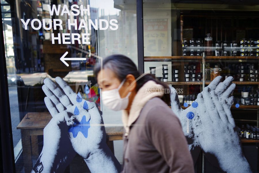 A woman wearing a face mask walks near a shop featuring a washing hands slogan Tuesday, April 14, 2020, in Tokyo. Japanese Prime Minister Shinzo Abe declared a state of emergency last week for Tokyo and some other prefectures to ramp up defenses against the spread of the coronavirus. (AP Photo/Eugene Hoshiko)