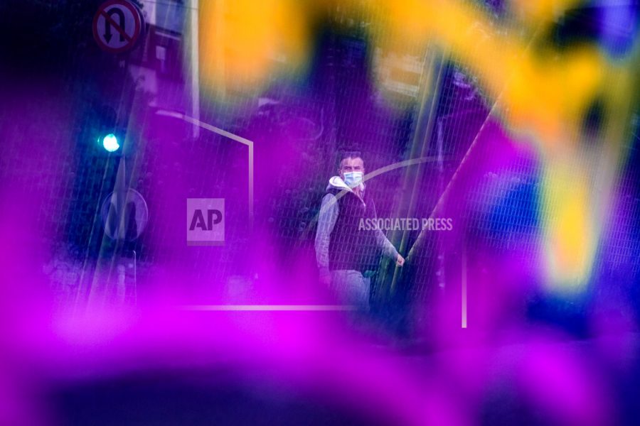 Seen through a bridge glass panel covered in graffiti a man wearing a face mask walks in Sarajevo, Bosnia, Wednesday, May 6, 2020. After nearly two months in lockdown, mosques in Bosnia have reopened to believers celebrating the islamic holy month of Ramadan, who can attend three daytime prayers as long as they observe social distancing rules and use protective equipment. (AP Photo/Kemal Softic)