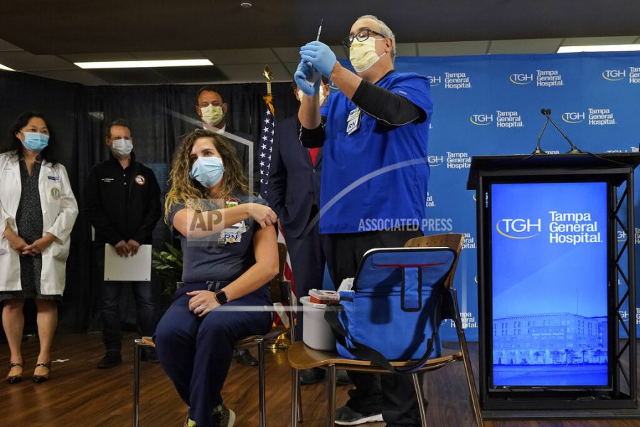 Nurse Vanessa Arroyo, seated, rolls up her sleeve as she prepares to get a COVID-19 vaccine shot from nurse Rafael Martinez during a news conference Monday, Dec. 14, 2020, at Tampa General Hospital in Tampa, Fla.  (AP Photo/Chris OMeara)