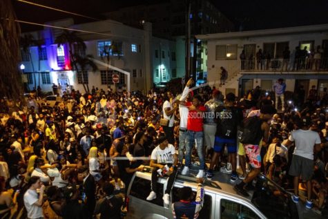 Crowds defiantly gather in the street while a speaker blasts music an hour past curfew in Miami Beach, Fla., on Sunday, March 21, 2021. An 8 p.m. curfew has been extended in Miami Beach after law enforcement worked to contain unruly crowds of spring break tourists.  (Daniel A. Varela/Miami Herald via AP)