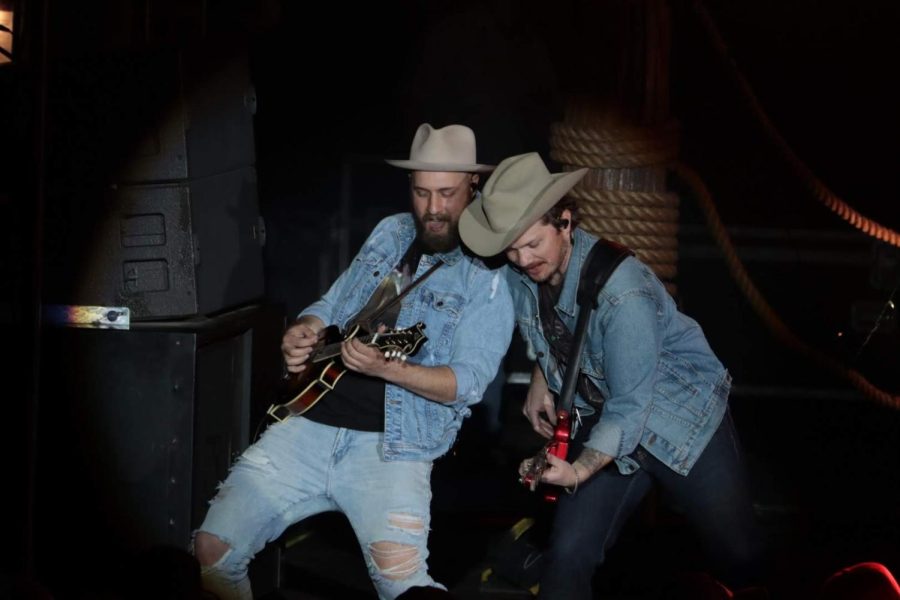 Two guitarists and singers wearing country hats perform on stage