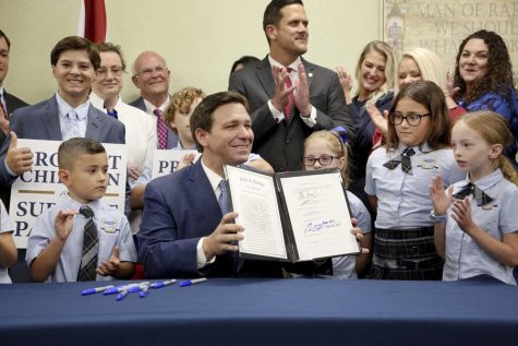 Florida Governor Ron DeSantis holds up the signed Parental Rights in Education bill, surrounded by elementary school children