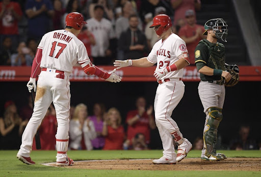 Los Angeles Angels' Mike Trout, center, is congratulated by Shohei Ohtani, left, of Japan, after hitting a two-run home run, while Oakland Athletics catcher Jonathan Lucroy stands at the plate during the third inning of a baseball game Friday, Sept. 28, 2018, in Anaheim, Calif. (AP Photo/Mark J. Terrill)