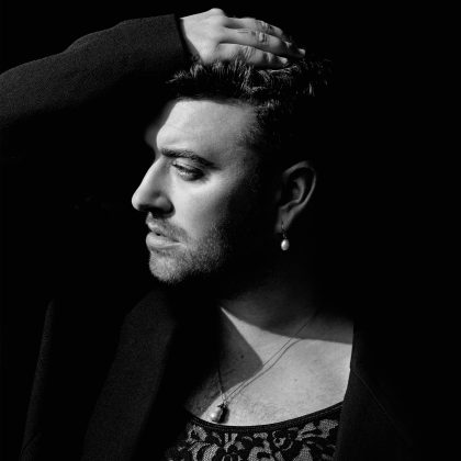 A black and white profile of Sam Smith with is hand on his head, sporting a peal earring and necklace. 
