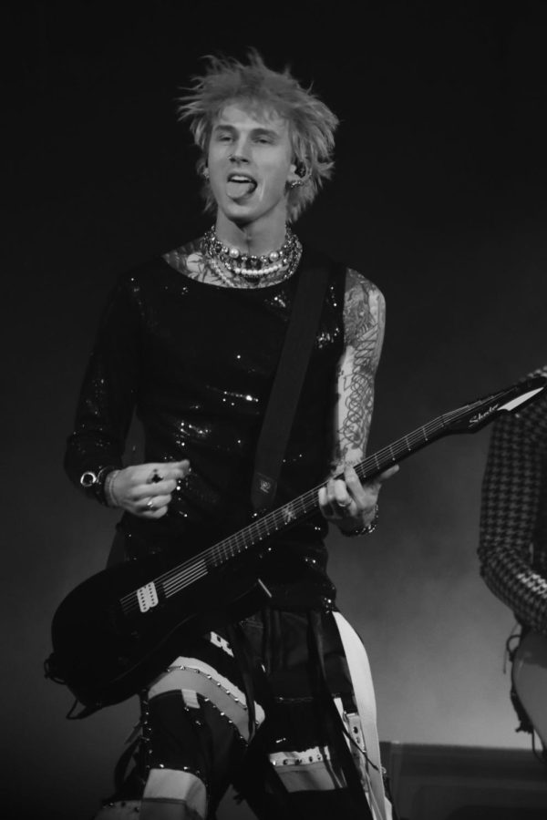 MGK sticks out his tongue while holding a guitar