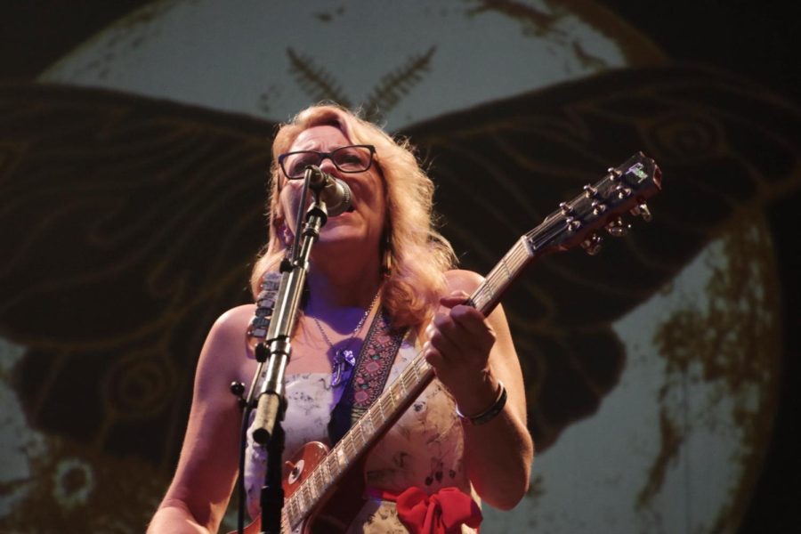 Susan Tedeschi sings into a microphone while playing guitar