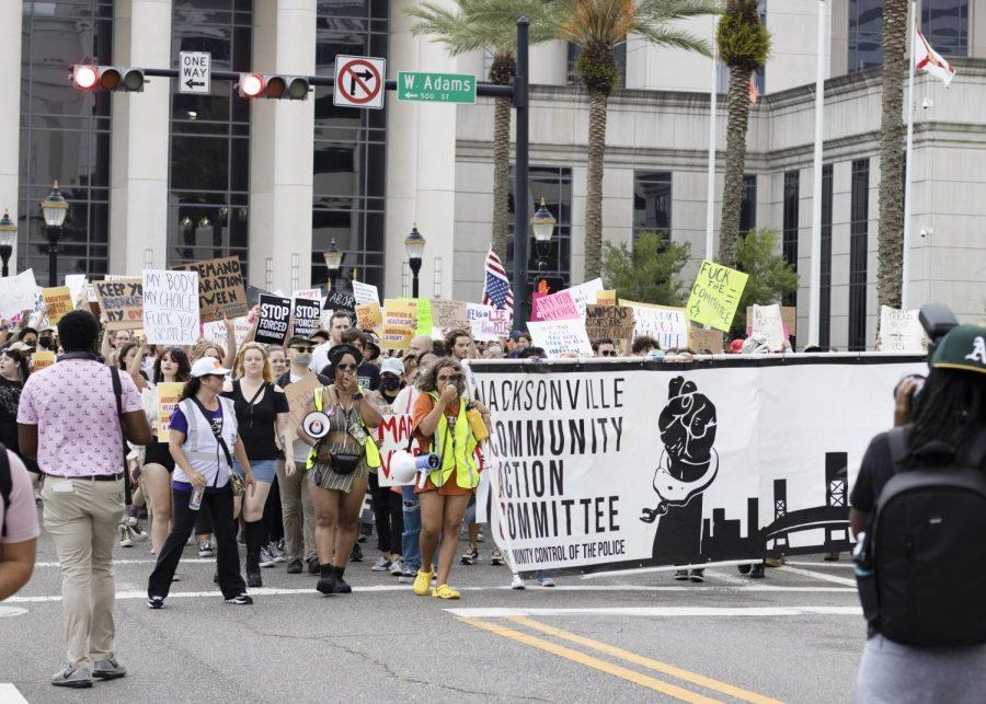 Protesters start their march, many of them holding signs and hoisting a large white banner