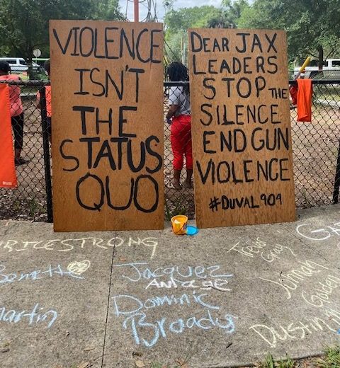 Signs protesting against gun violence stand in Success Park during a volunteer clean-up event