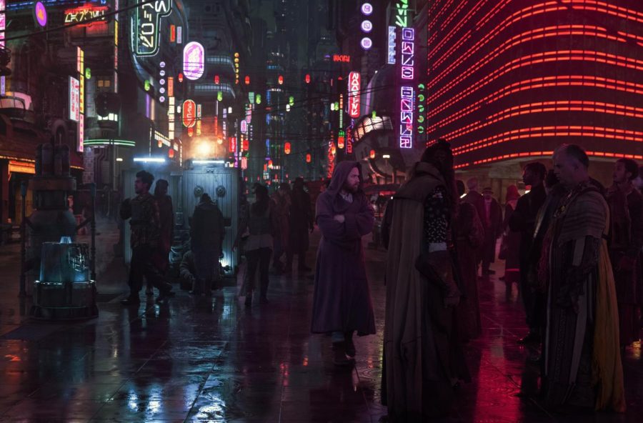 People walk up and down a street in a city lit by numerous neon signs