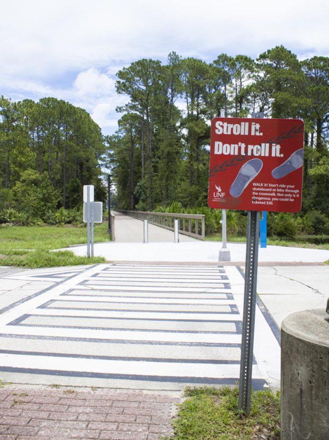 A red stroll it. dont roll it no skateboarding sign is posted in front of a long boardwalk cutting between the forest to the parking lot