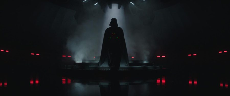 Darth Vader steps off a stage, silhouetted with a dim light