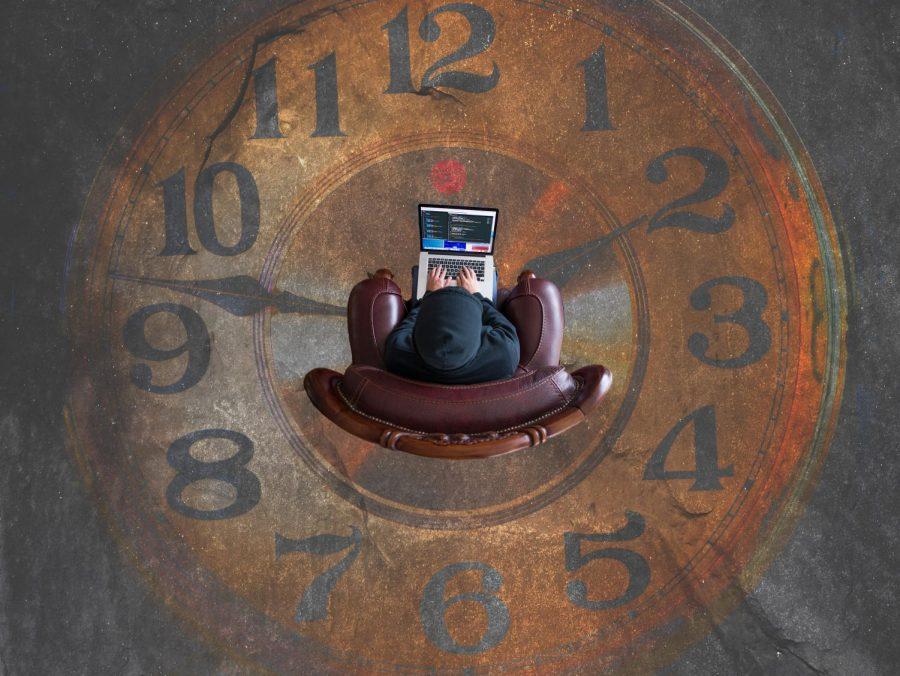 An overhead shot of a person on a laptop. The floor is an analog clock