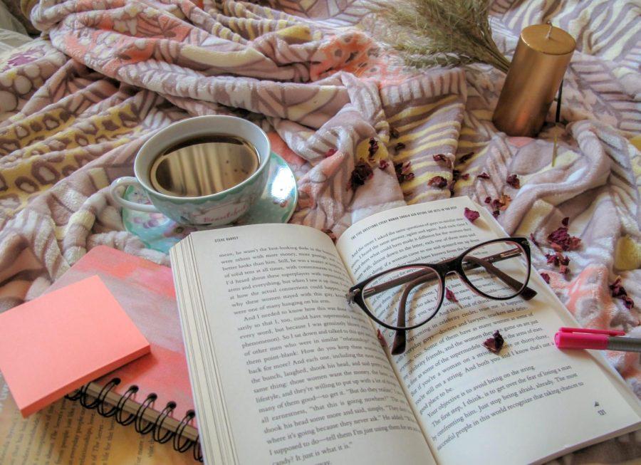 A cup of tea, a candle, post its, and glasses sit on and around an open book