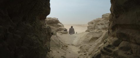 Obi Wan Kenobi sits on a hill in the sand with his back to the camera