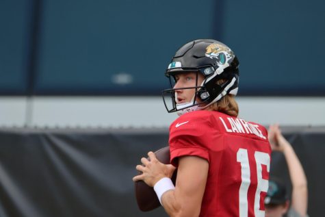 Trevor Lawrence in a red uniform and black helmet gets ready to throw a football