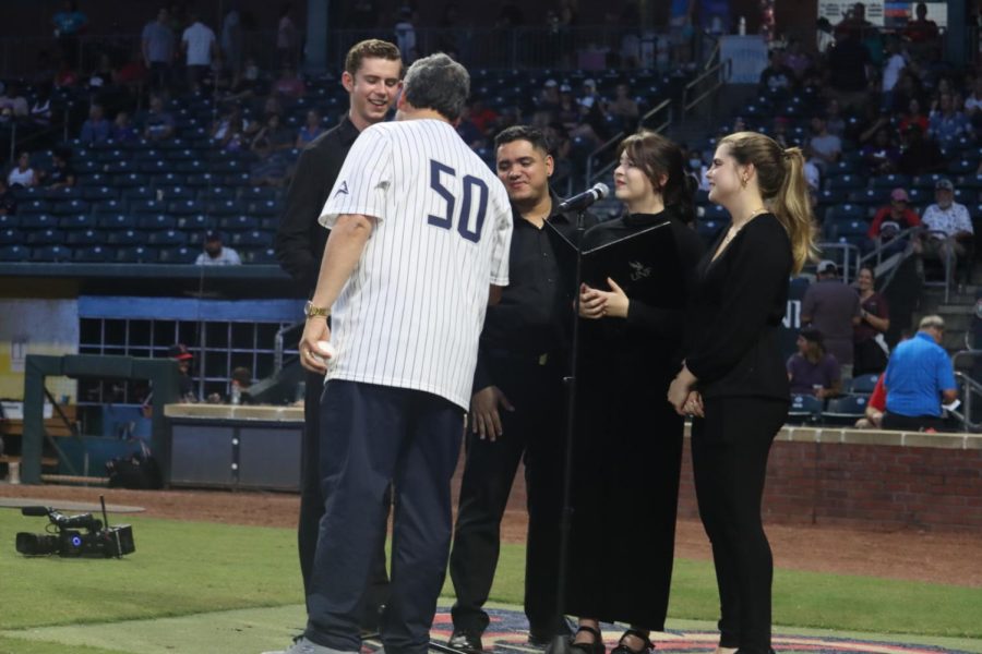 Limayem wears a white striped jersey with the number 50 on the back. He stands next to 4 members of the UNF chamber singers wearing all black