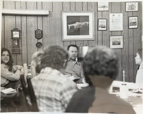 A black and white photo of students and Roach sitting around a table during a meeting