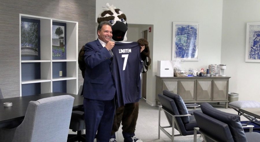 Limayem stands with a blue suit holding a blue and white basketball jersey with LIMAYEM and 7 on it with Ozzie the Osprey
