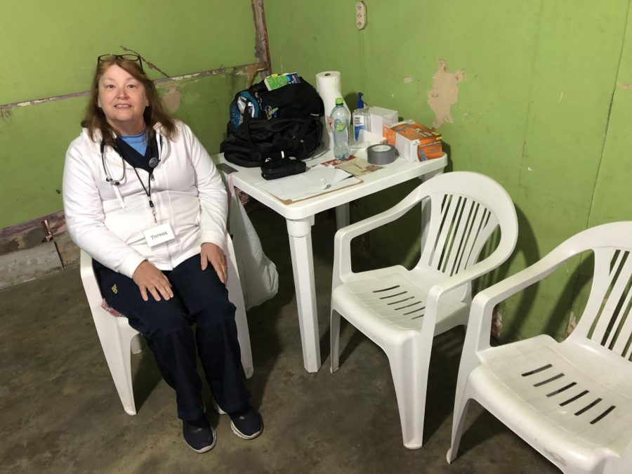 Teresa Steele sits in a white plastic chair, wearing a white hoodie and black pants. next to a table with her gear