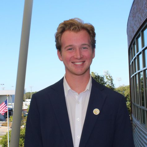 Michael Barcal smiles for a photo wearing a blue suit jacket, white button down and an SG button