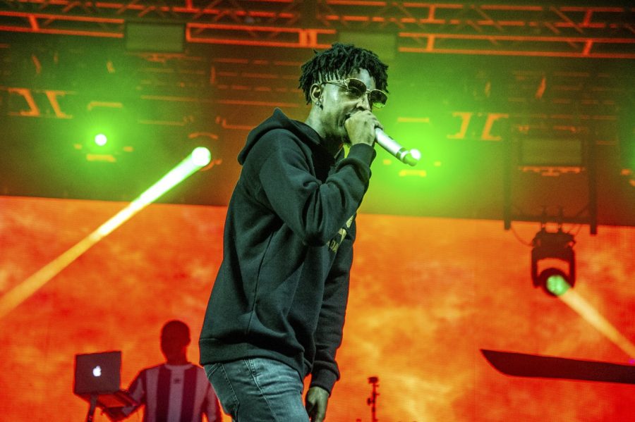 21 Savage performing wearing all black, black sunglasses and holding a microphone