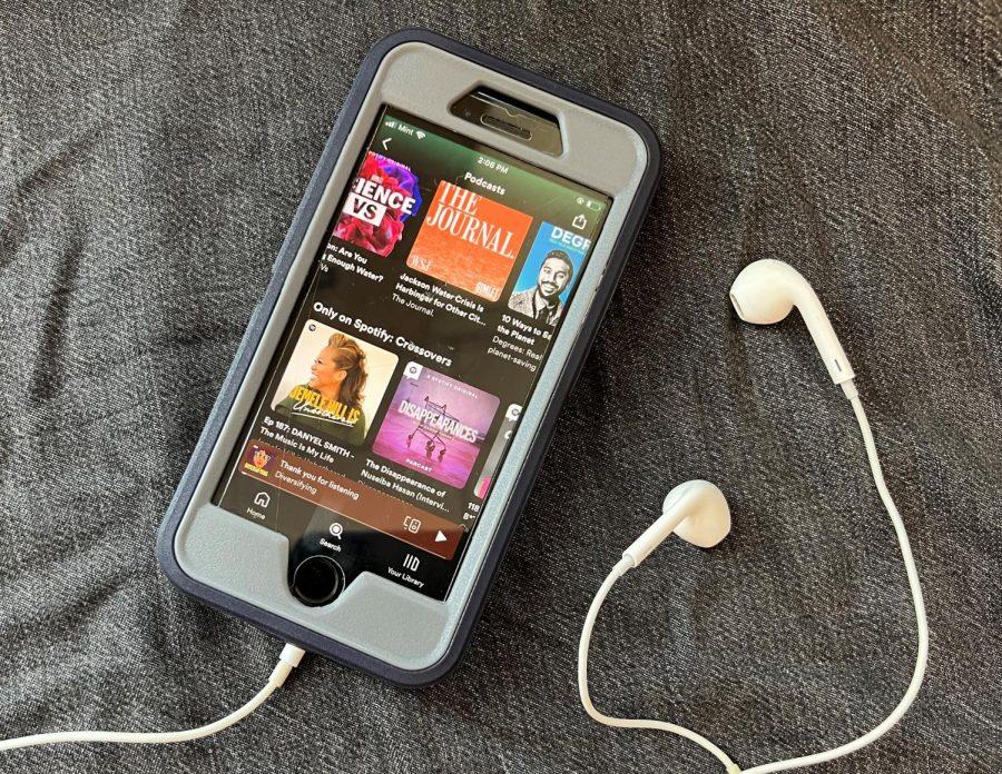 An iPhone with headphones with podcasts open on Spotify