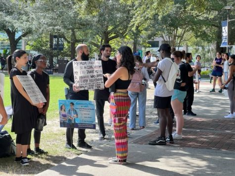 students talk and debate with preachers on the edge of the green holding large signs with often profane messages on them