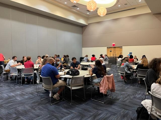 Students sit around multiple round tables, talking