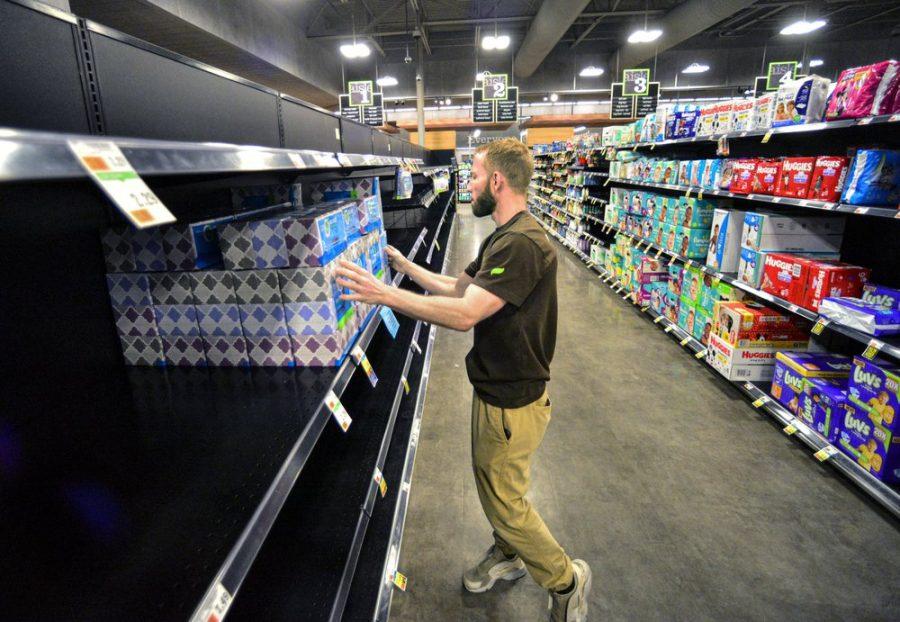 A man grabs tissues off the shef of a store with many empty shelves