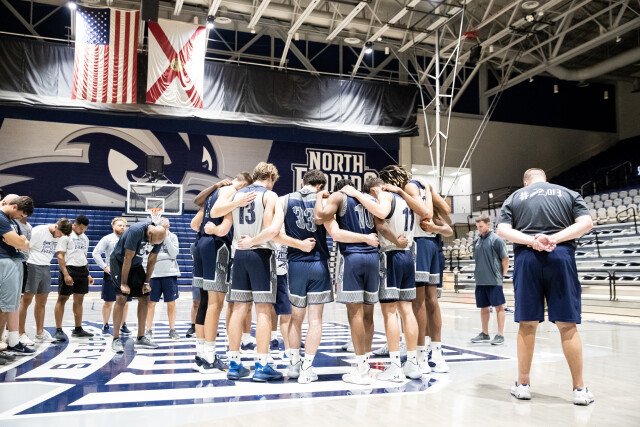 Men's basketball players huddle together during practice.