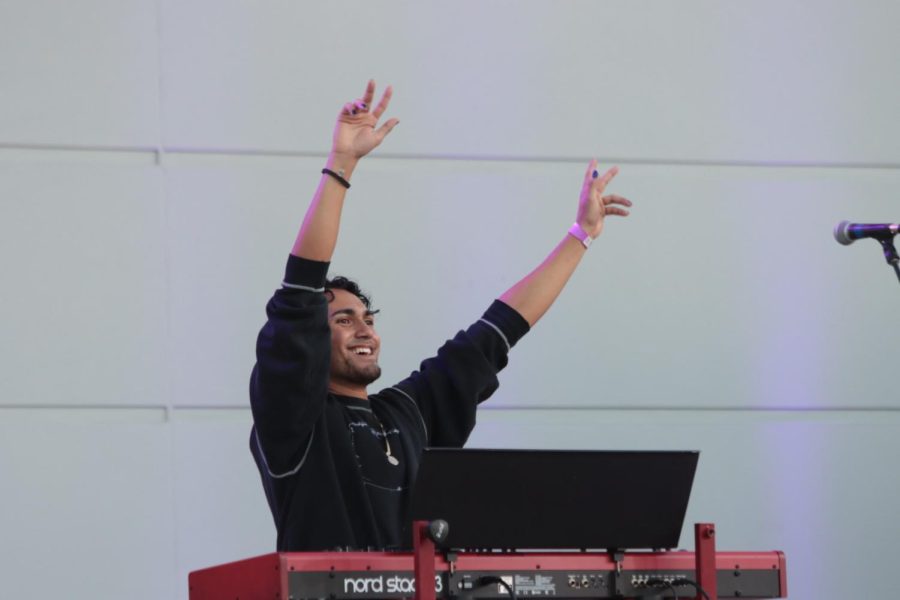 Samuel smiles, raising his hands in the air with peace signs while performing