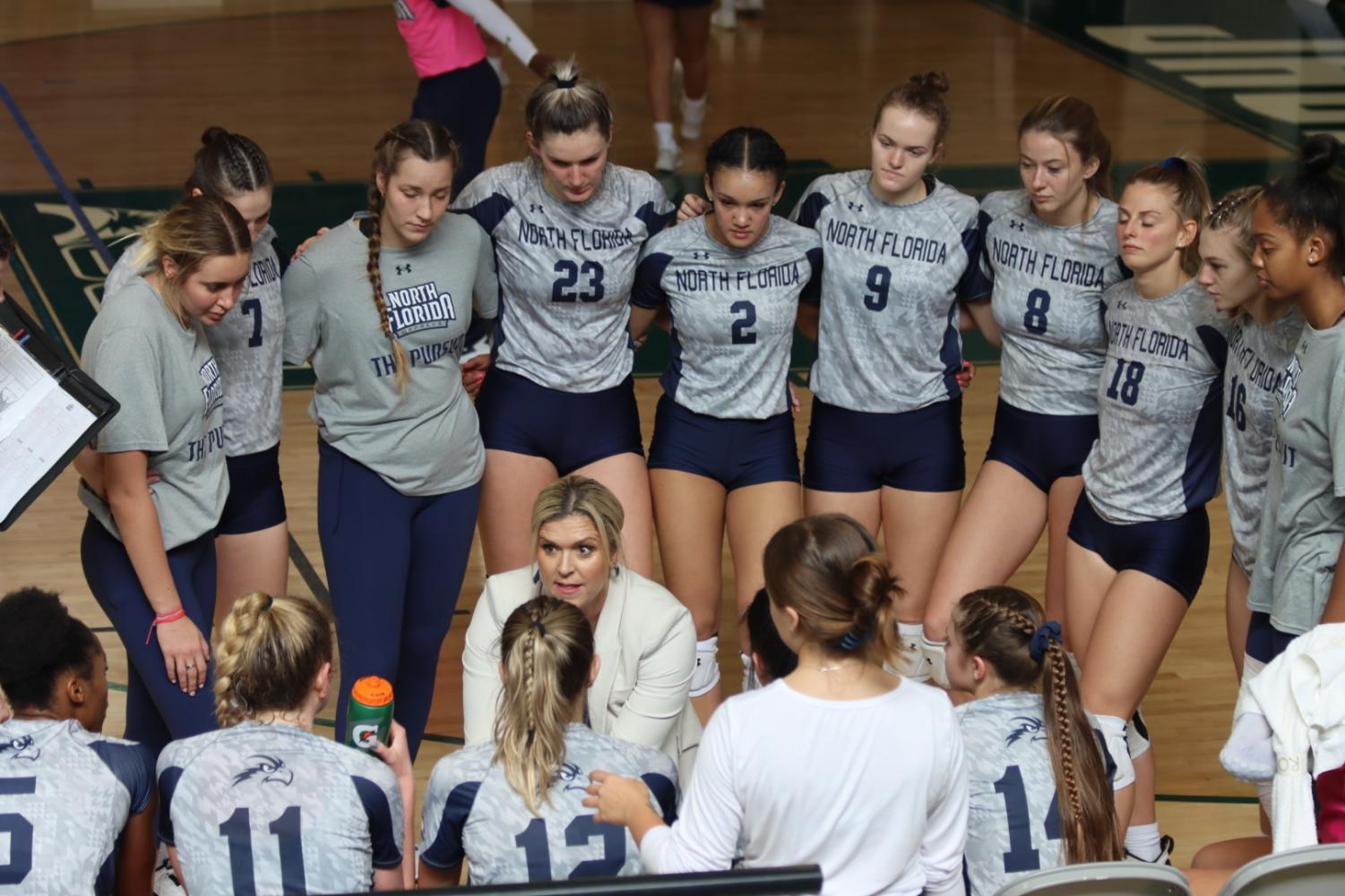 Volleyball team huddles around their head coach.