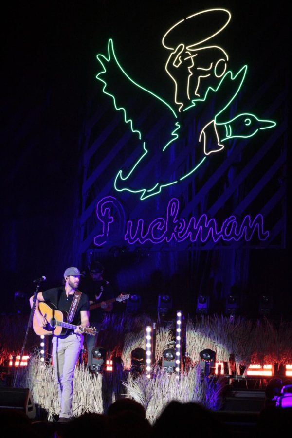 Riley Green sings in front of a giant neon Duckman sign