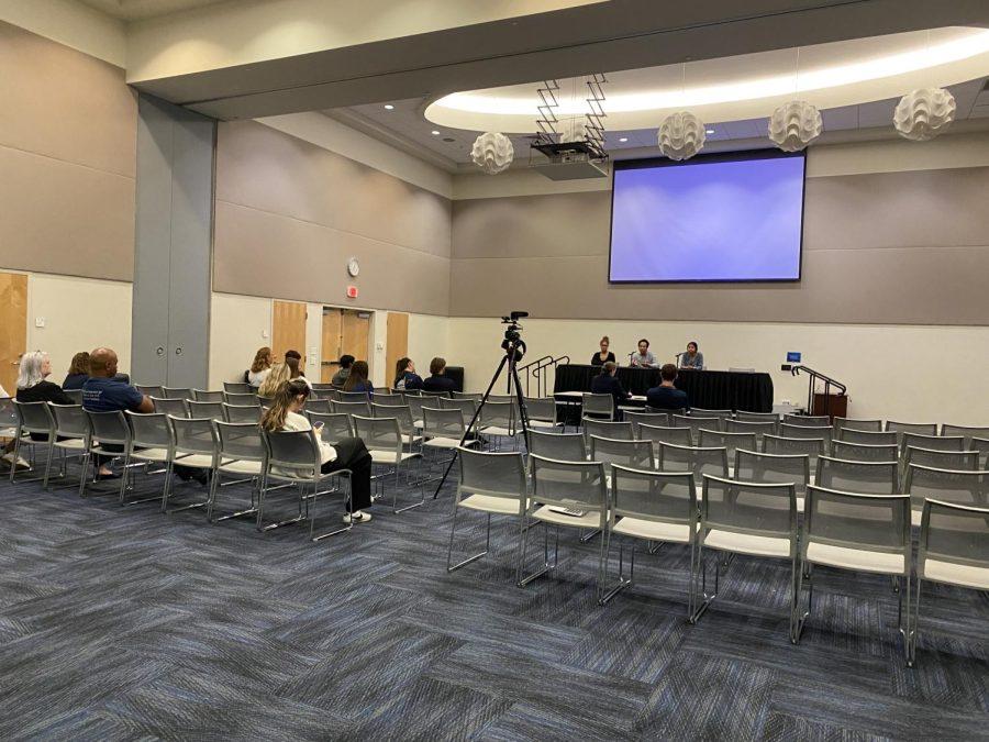 Candidates sit behind a black table in front of rows of empty chairs