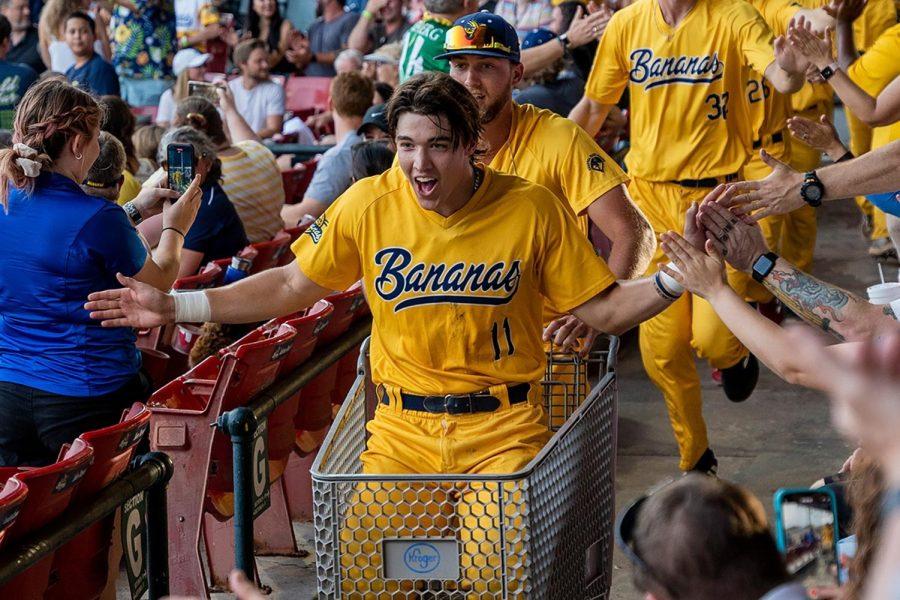 Baseball player pushed by teammates in a shopping cart through the crowd