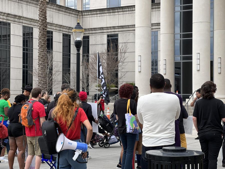 Protesters stand away from the camera, looking at a speaker in the back of the photo.