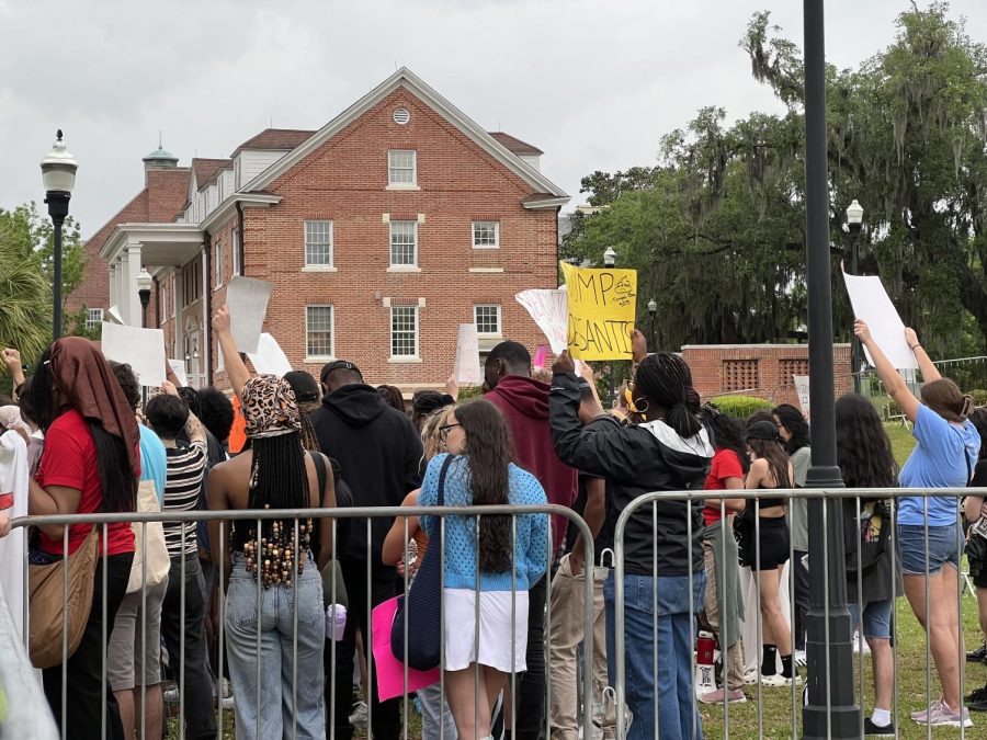 Protesters stand behind metal fences, holding signs and chanting loudly across the street on Tuesday.