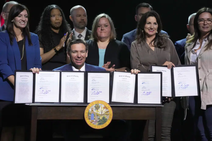 Florida Gov. Ron DeSantis holds up bills he signed during a bill signing ceremony at the Coastal Community Church at Lighthouse Point, Tuesday, May 16, 2023, in Lighthouse Point, Fla. (AP Photo/Wilfredo Lee)