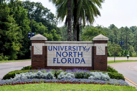 The University of North Florida entrance sign with a green palm tree behind and purple and white flowers in front.