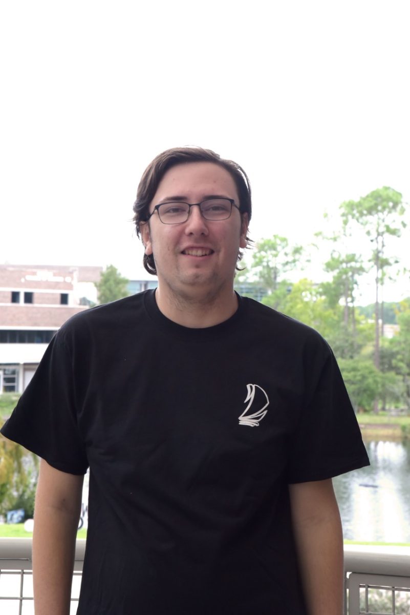 Ethan has brown hair and is smiling for a photo, wearing a black t-shirt