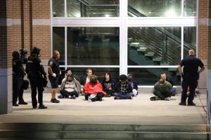 Officers stand as protesters sit in custody. 