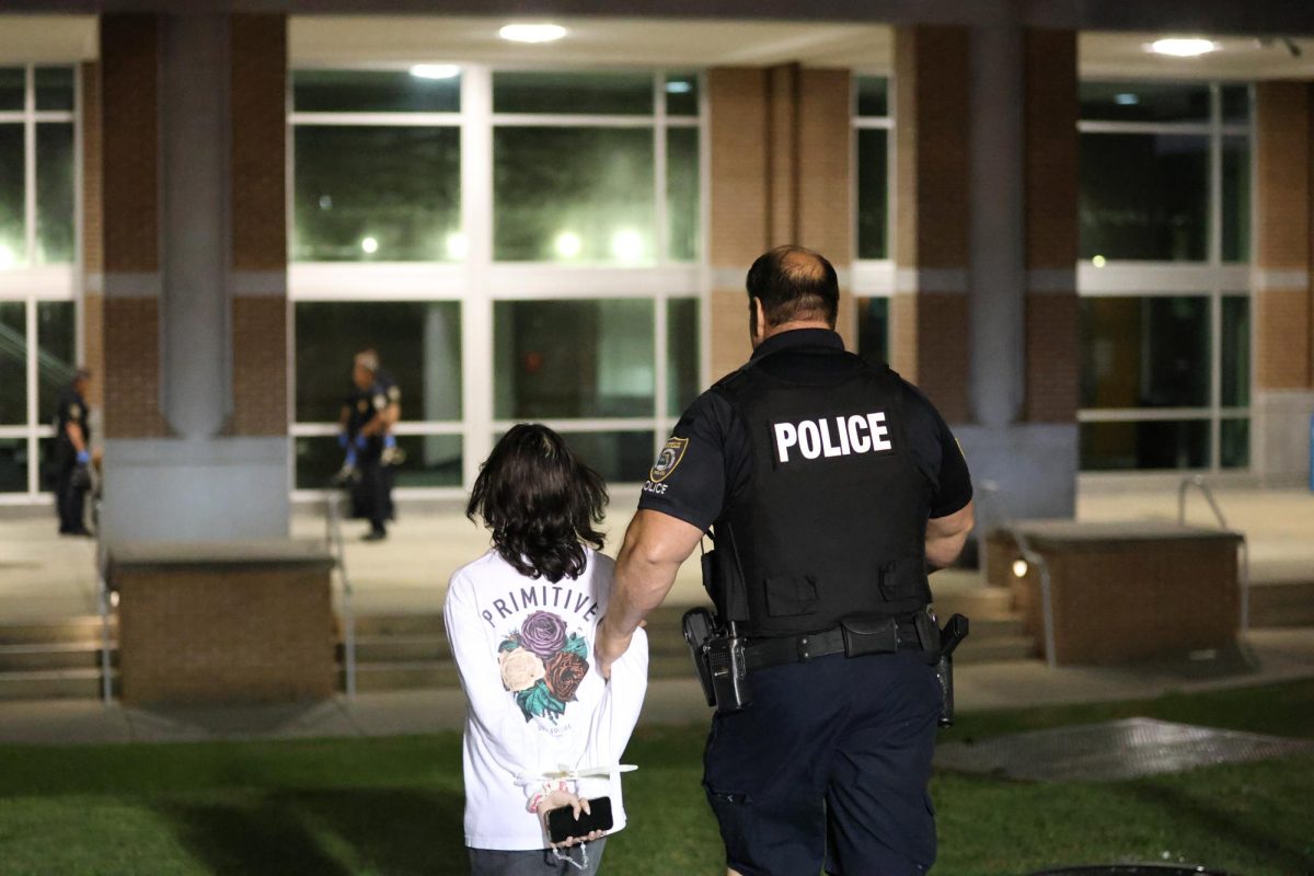 An officer walks a protester to sit along the Fine Arts Center. 