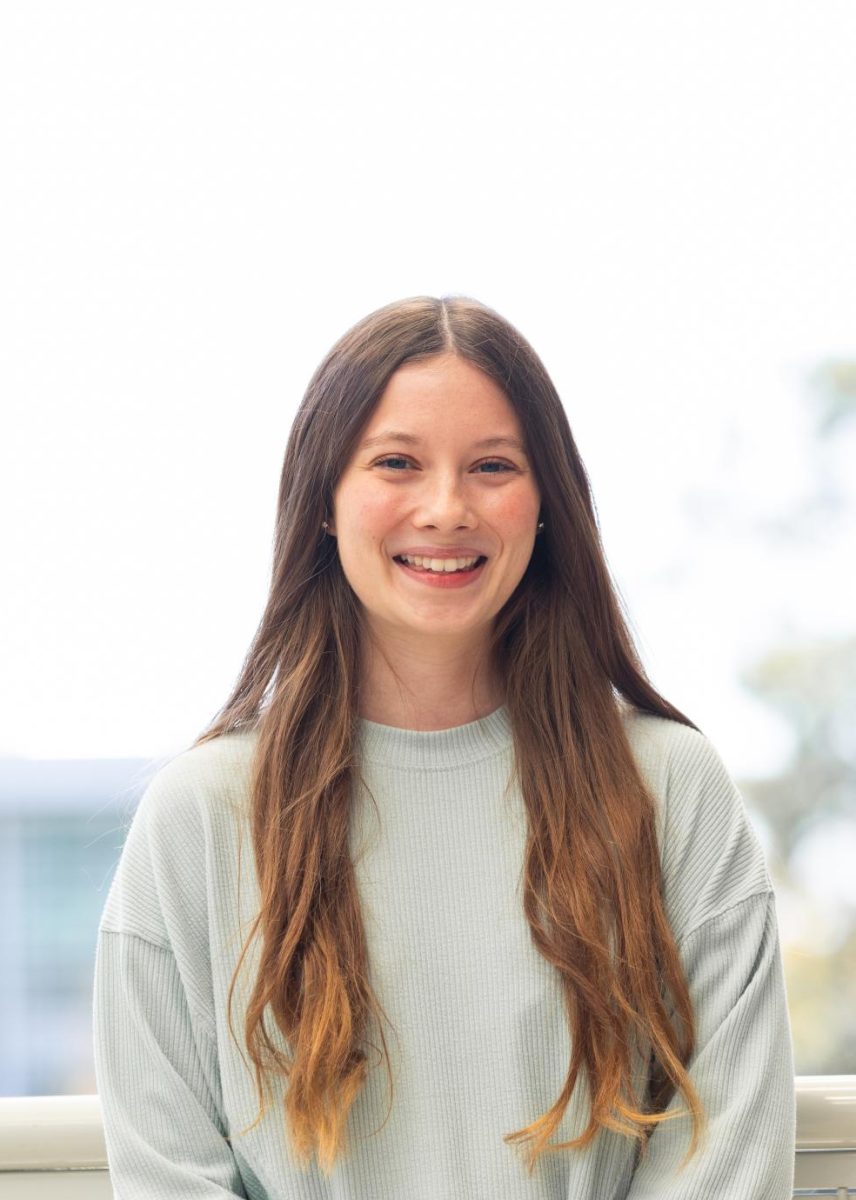 Savanna is wearing a light green sweatshirt and black pants and is smiling. She has long, light brown hair.