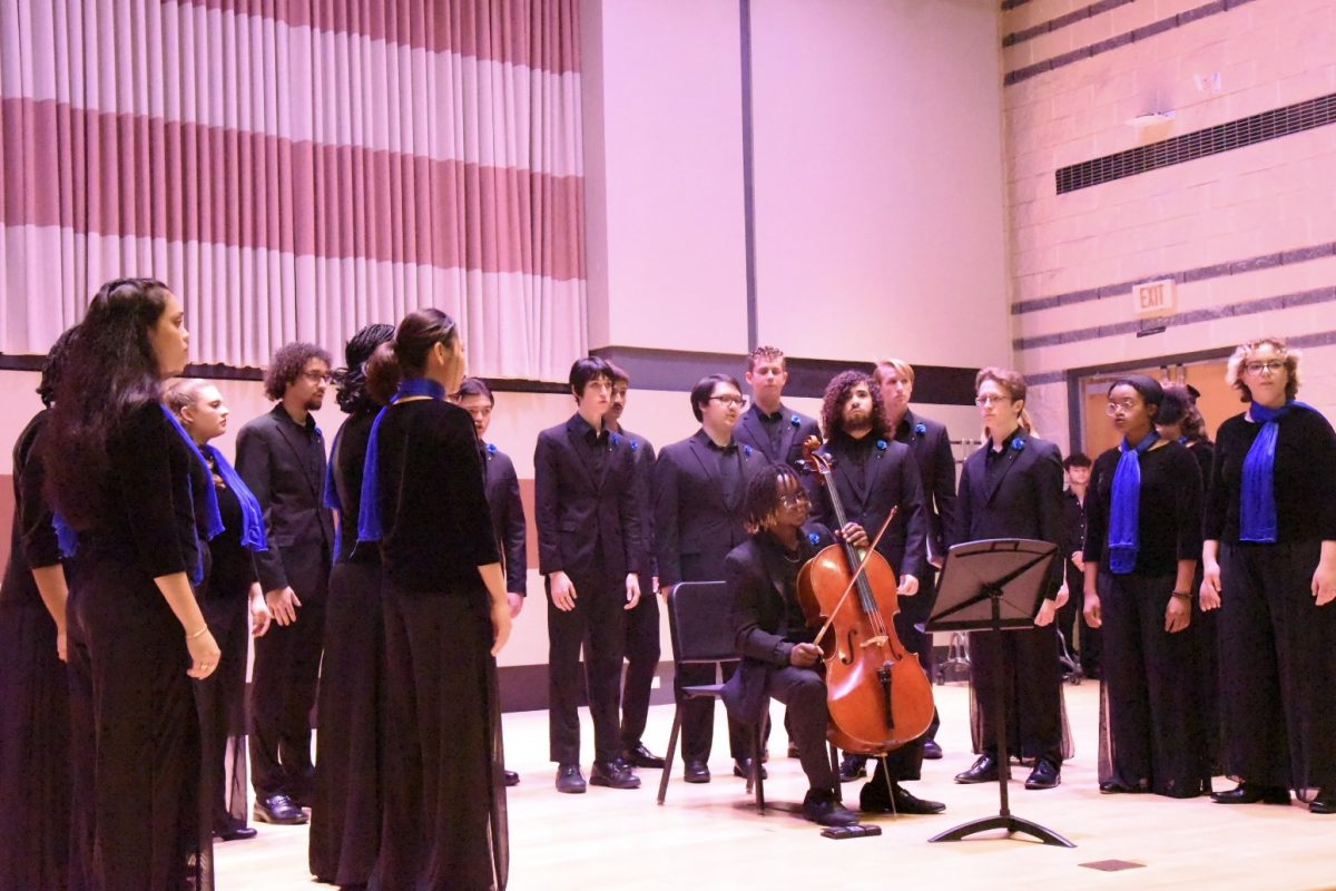 The UNF Chamber Singers stand and sing in an arc shape in their black uniforms and blue scarves at the UNF Recital Hall