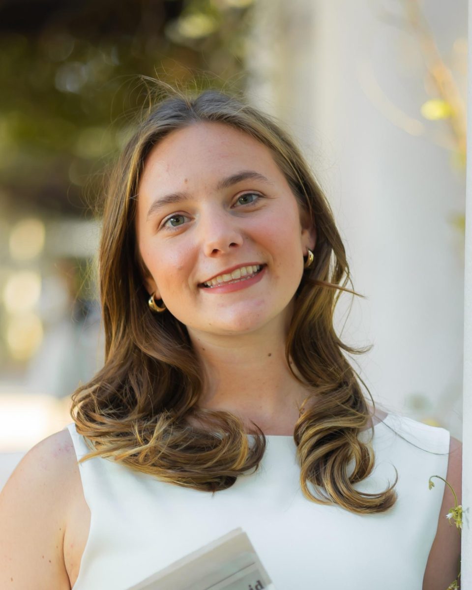 Abigail is smiling for a photo and has light brown hair and is wearing a white shirt