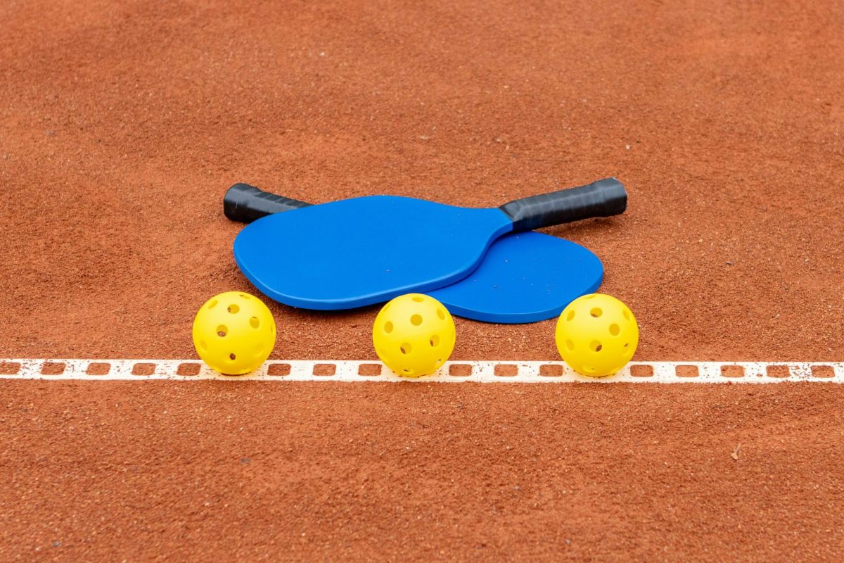 Two paddles and three pickleballs on a court. (Aleksander Saks/Unsplash)